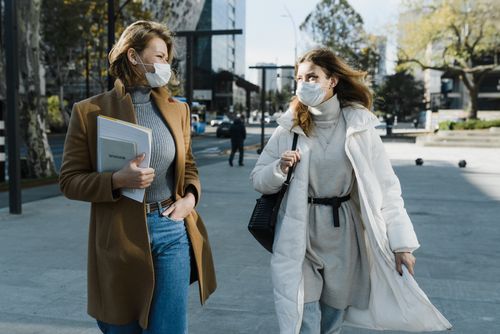 Free Two women wearing face masks and winter coats walking outdoors in a city setting. Stock Photo