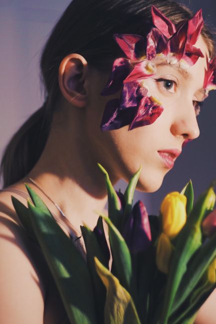 A unique side-profile portrait of a woman with floral art on face, holding tulips.