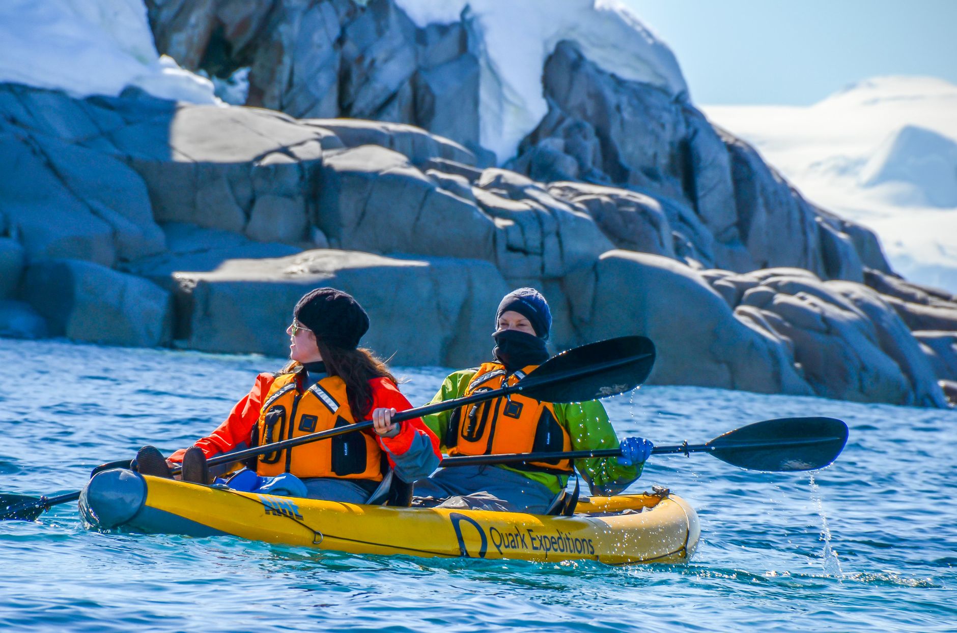 Two adventurers kayaking in the icy waters of Antarctica, surrounded by stunning rocky landscapes.