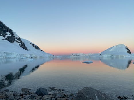 A calm sunset reflecting over icy waters and glaciers in Antarctica.