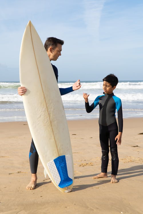 A Kid Standing Next to a Man Holding a Surfboard while Standing on the Shore