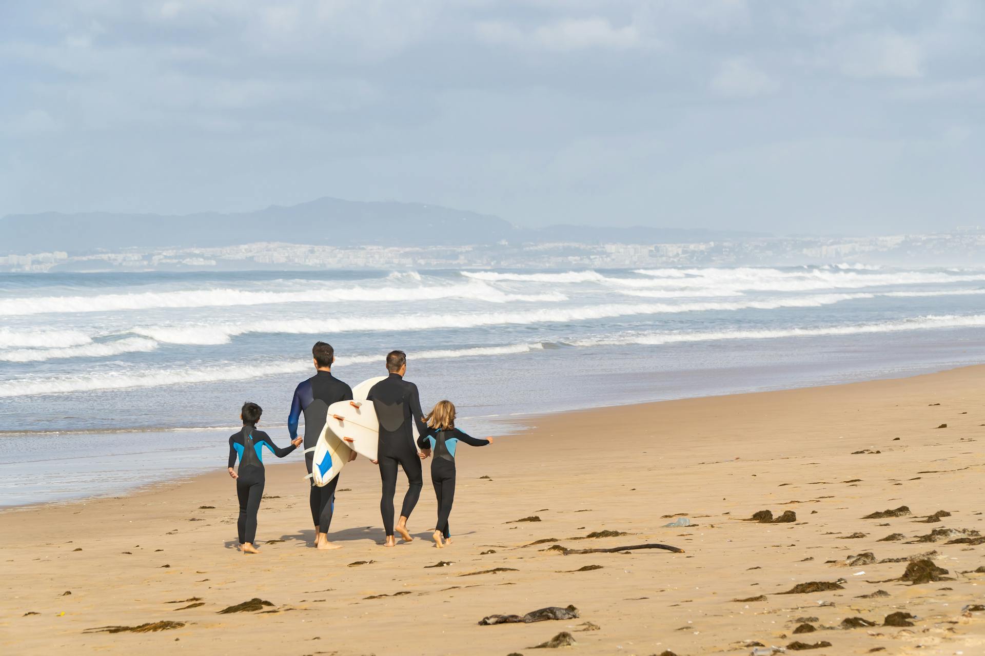 A family enjoys a day surfing on a beautiful Portuguese beach, carrying surfboards along the shoreline.