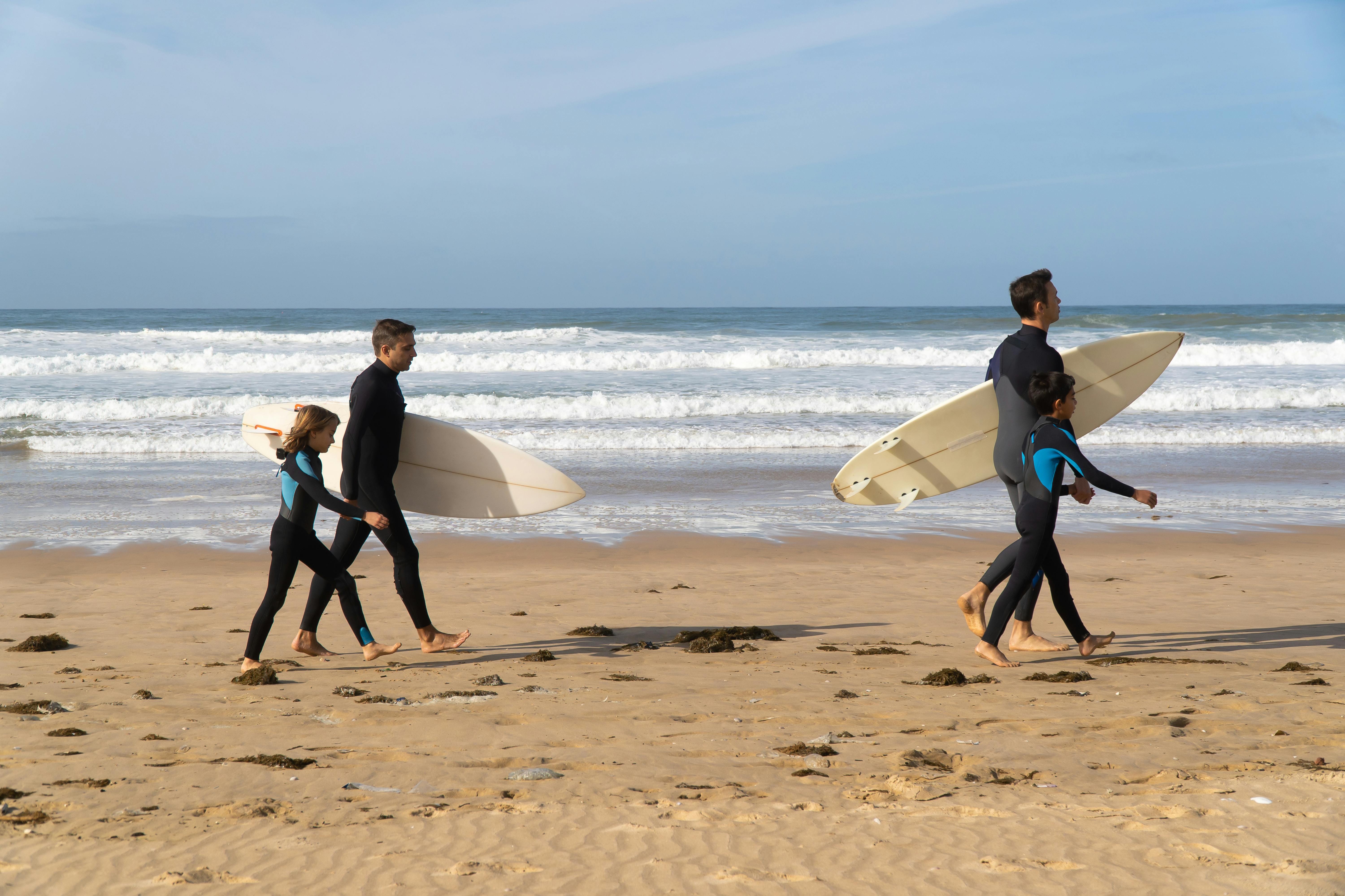 Family walking with surfboards on a sunny beach in Portugal, enjoying a surfing adventure.