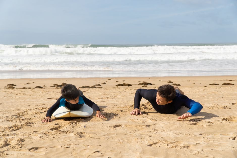 A man teaching a boy surfing techniques on a sunny beach in Portugal, enjoying the waves.