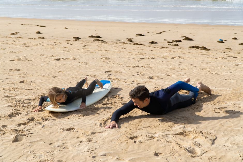 A man teaching a young girl how to surf on the sandy beach in Portugal.