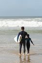 Man Holding Surfboard Beside a Boy at the Beach