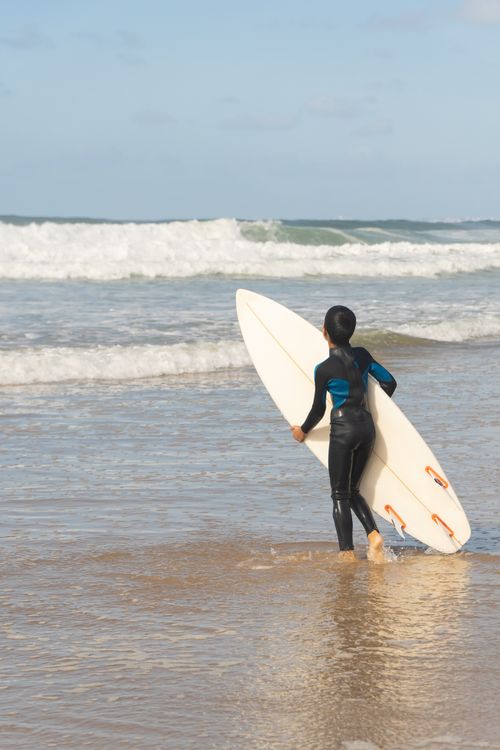 Free Boy in wetsuit holding surfboard at the beach in Portugal, exploring surfing. Stock Photo
