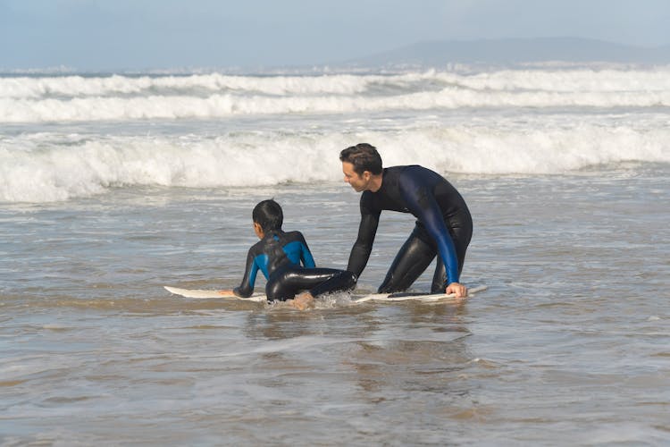 Man Teaching A Boy How To Surf