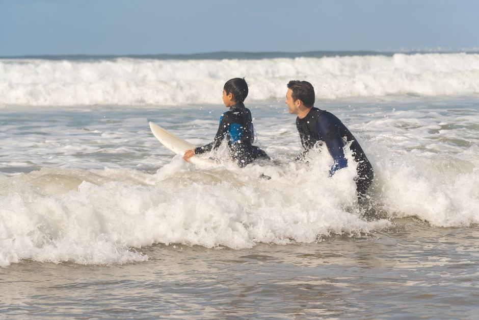 A father and son bond while surfing the waves on a sunny day in Portugal.