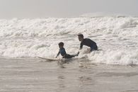 Photo of Man Guiding a Boy in Surfing Sea Waves