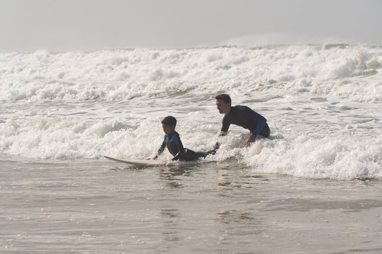 Photo Of Man Guiding A Boy In Surfing Sea Waves