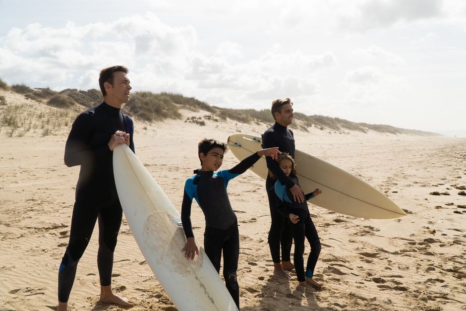 Two men and children with surfboards on a sandy beach in Portugal.