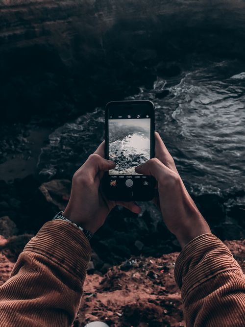Free Hands capturing a rugged Moroccan coastline with a smartphone from above. Stock Photo
