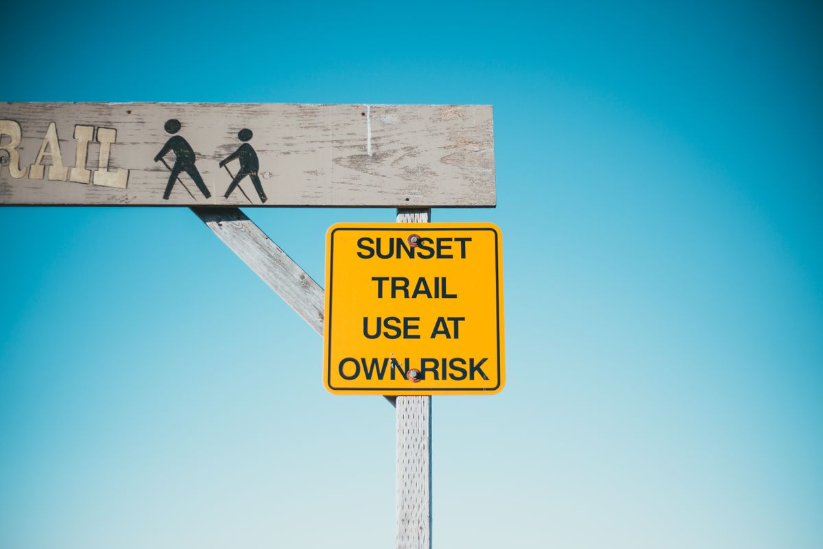 Yellow warning signboard under a wooden arch against a blue sky