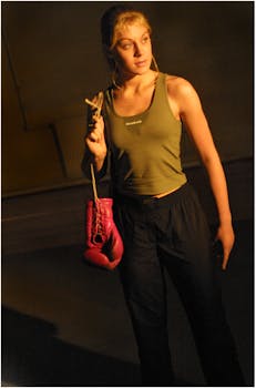 在室内阴沉的灯光下，一位时尚女性戴着拳击手套，姿态轻松