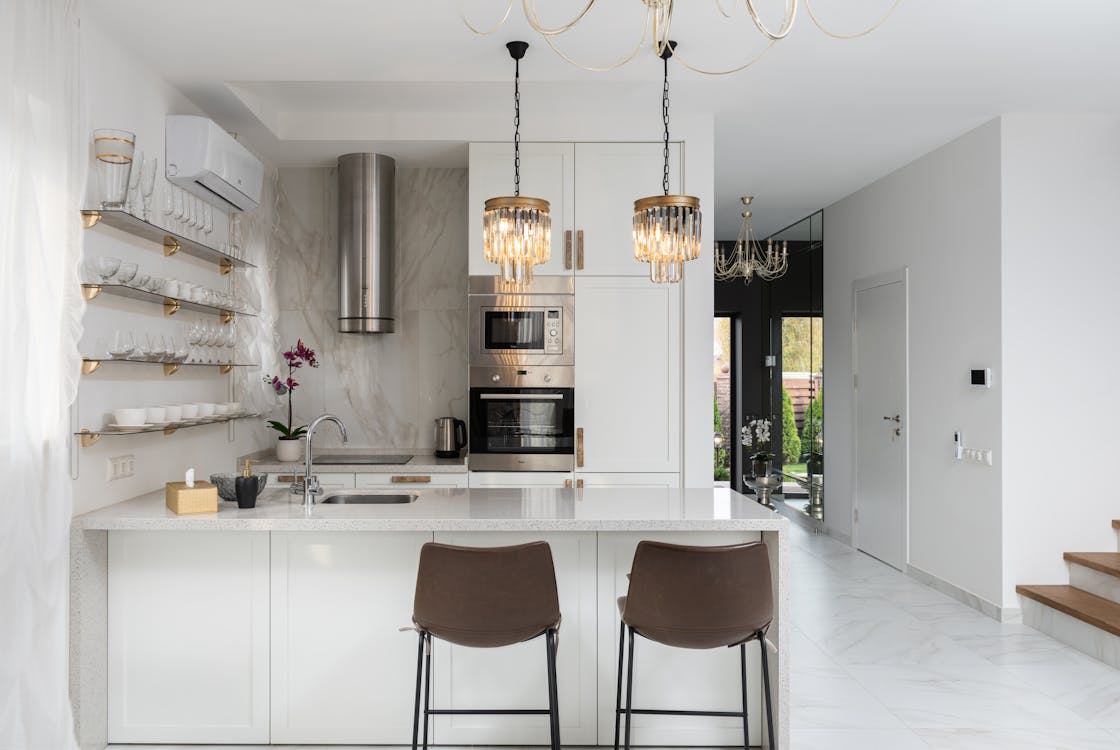 Free Interior of contemporary kitchen with modern appliances and chairs at white counter near wall with shelves in spacious apartment near stairs Stock Photo