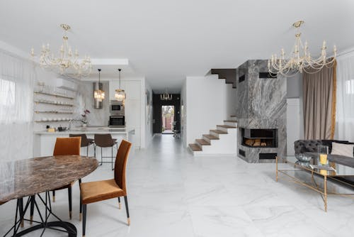 Stylish apartment with chairs at table placed near white kitchen counter in room with couch and side table near fireplace at staircase