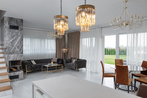 Interior of modern apartment with chairs at table placed in room with soft sodas near big windows with curtains and fireplace