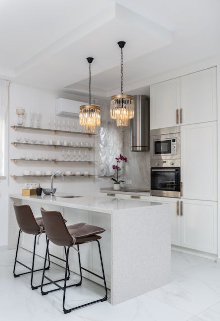 Modern white kitchen with chairs and potted flower near contemporary kitchenware and glassware on wall in apartment with glowing lamps