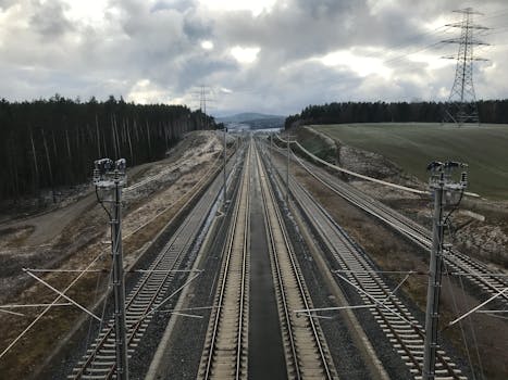 An aerial shot of railway tracks stretching through the countryside under cloudy skies.