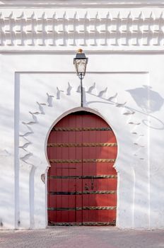 Exterior of traditional Islamic styled building with wooden arched door and vintage lamp hanging on white wall on sunny day in Marrakesh