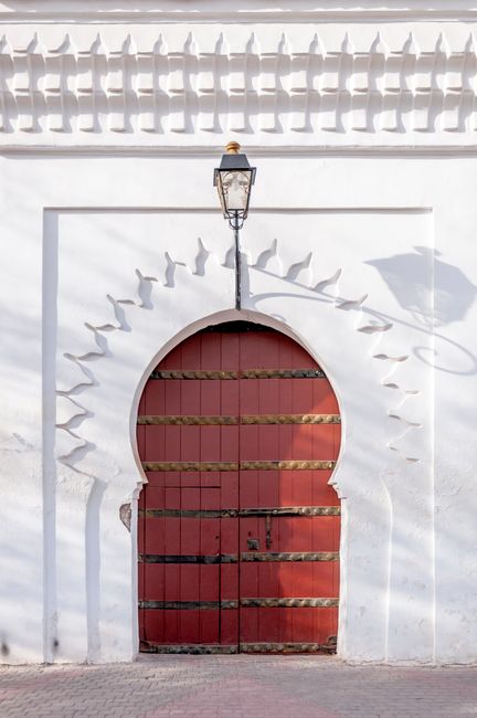 Exterior of traditional Islamic styled building with wooden arched door and vintage lamp hanging on white wall on sunny day in Marrakesh
