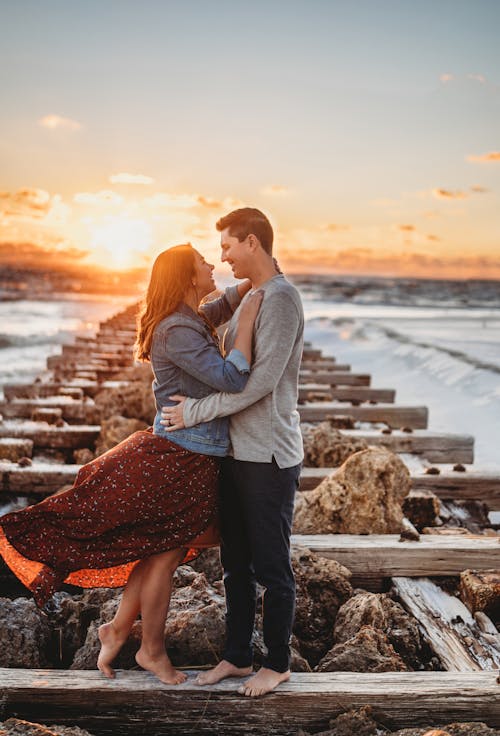 Free Romantic couple embracing on wooden pier at sunset Stock Photo