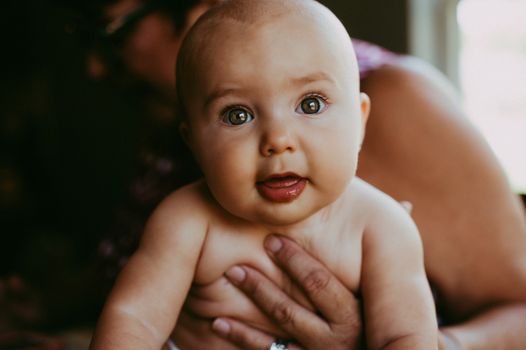 Crop unrecognizable grandmother hugging adorable newborn baby looking at camera in bedroom