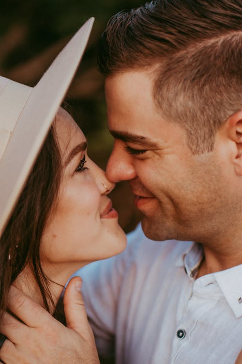 Side view of crop young loving couple in stylish outfits hugging and touching with noses before kissing in nature at sunset