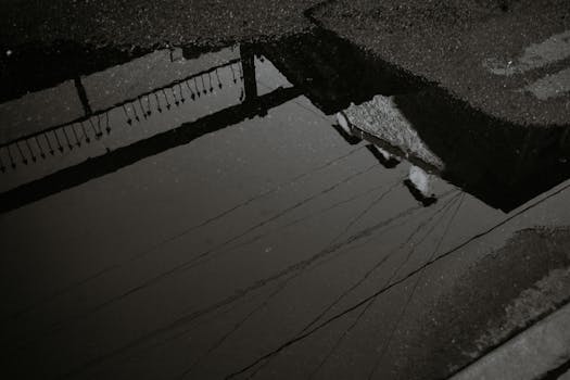 Moody black and white reflection of a cityscape in a rain puddle.