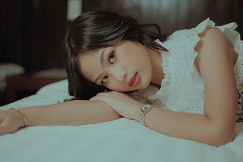 Free Calm young Asian woman with dark hair in stylish clothes lying on soft bed and looking at camera Stock Photo