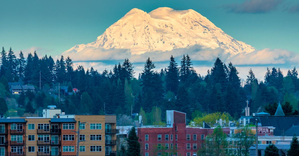 Majestic view of Mount Rainier with snow-capped peak rising behind urban buildings and dense forest.