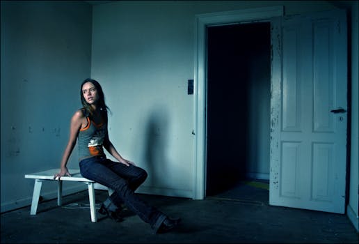 一名年轻女子独自坐在光线昏暗的废弃房间里，门敞开着，营造出一种神秘的氛围