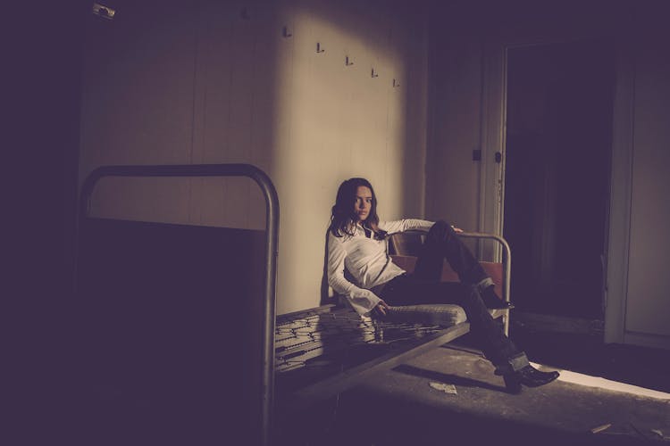 Woman Sitting On Bed Inside Empty Room