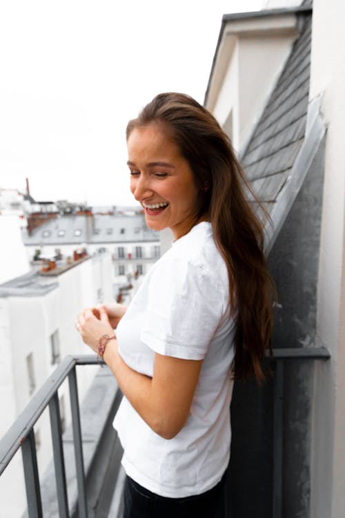 Young cheerful lady standing on balcony and enjoying city view