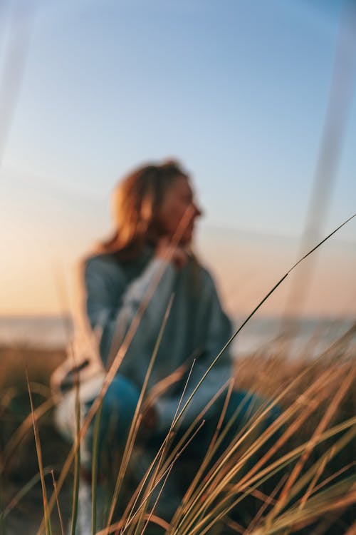 Unrecognizable woman recreating in meadow near seashore at sundown