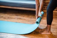 Crop unrecognizable ethnic woman in leggings preparing yoga mat for training in studio in daytime