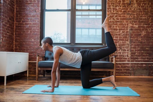 Side view full body of slim African American lady in sportswear doing Table pose in yoga on blue mat in light apartment near cabinet and couch near window in daylight