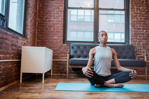 Full body of focused African American female in activewear practicing Sukhasana during yoga session on sports mat