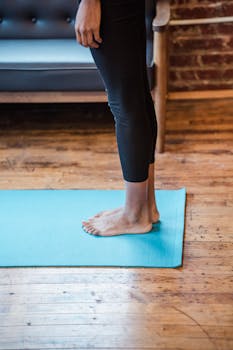 Woman in black leggings stands barefoot on a yoga mat indoors, highlighting a healthy lifestyle.