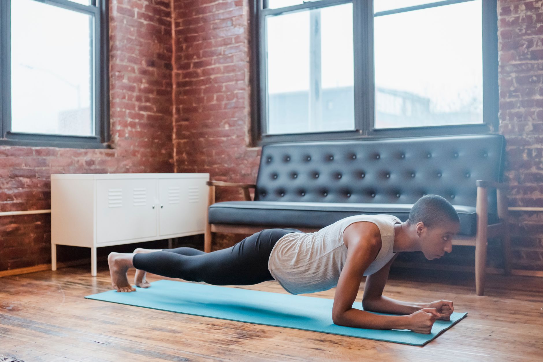 Full body side view of determined African American female in activewear practicing Phalakasana posture on mat during yoga training at home