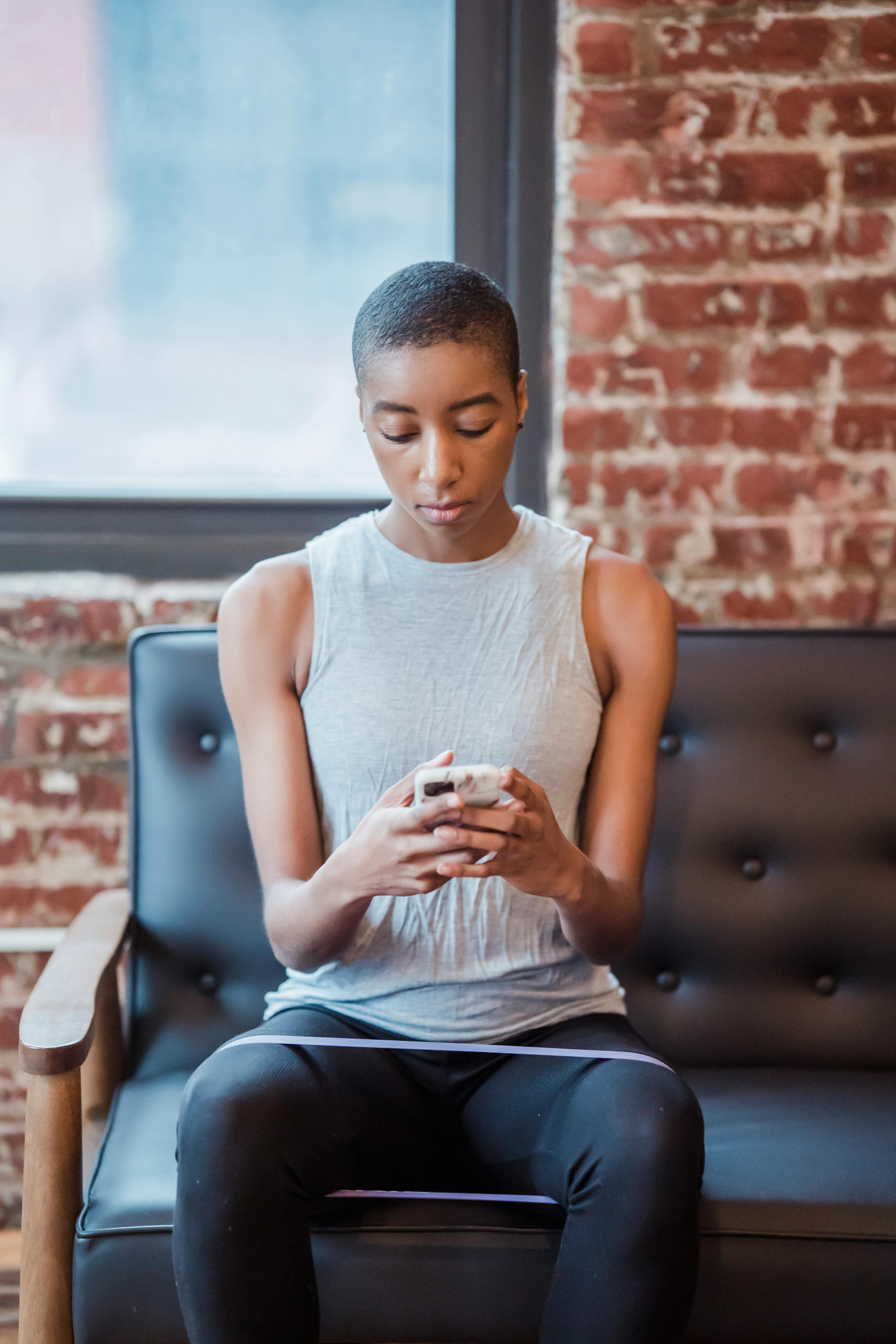 concentrated black sportswoman browsing smartphone during training with fitness expander