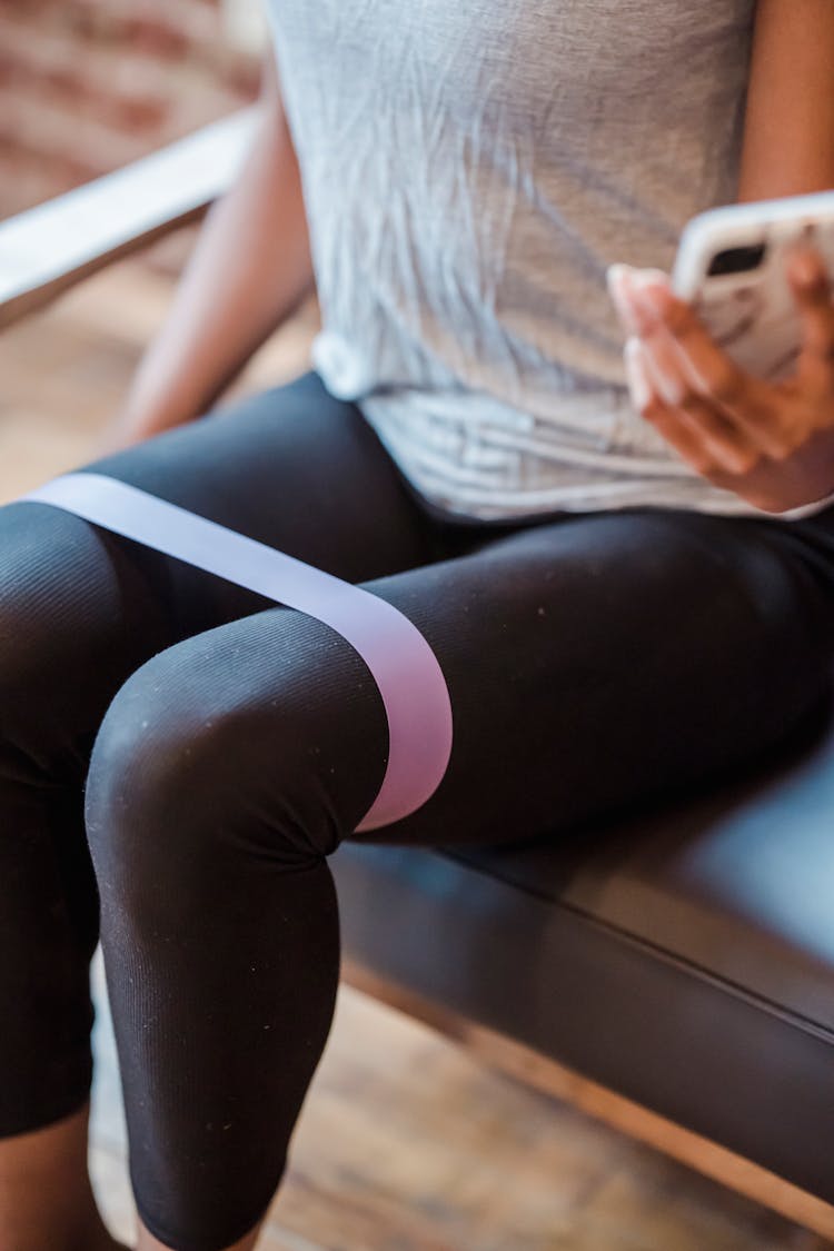 Crop Sportswoman Browsing Smartphone While Training With Resistance Band