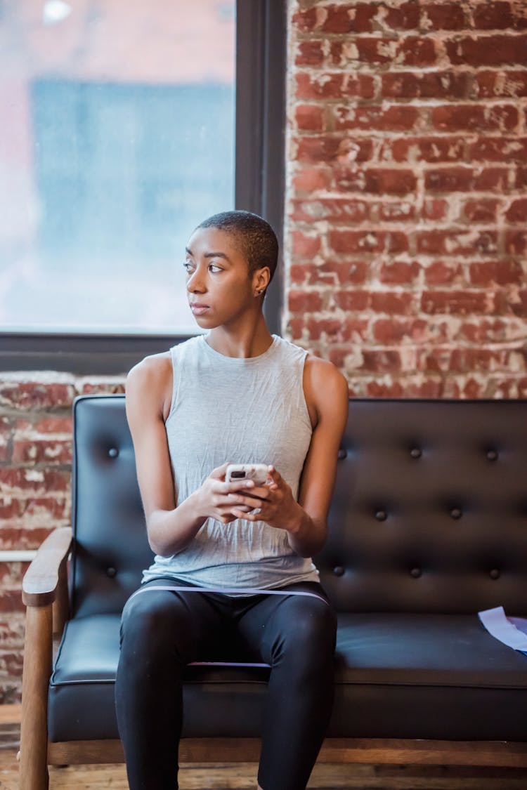 Thoughtful Black Woman With Smartphone Exercising With Elastic Band