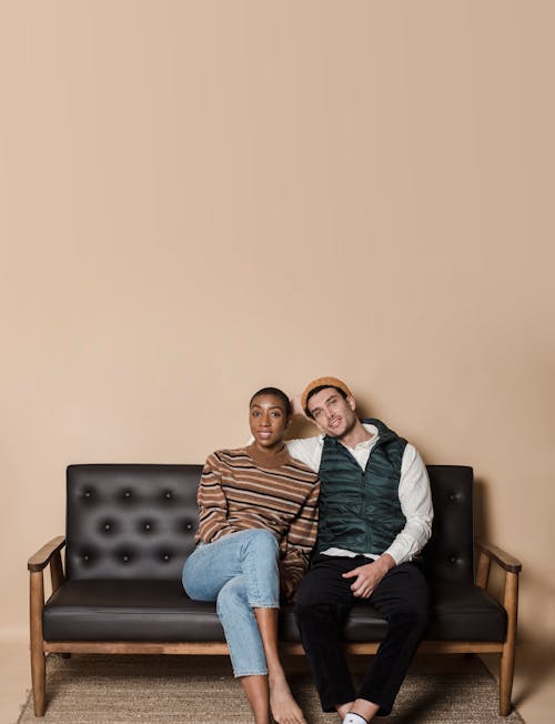 Cheerful African American girlfriend and boyfriend in casual clothes looking at camera while sitting on couch in room at home