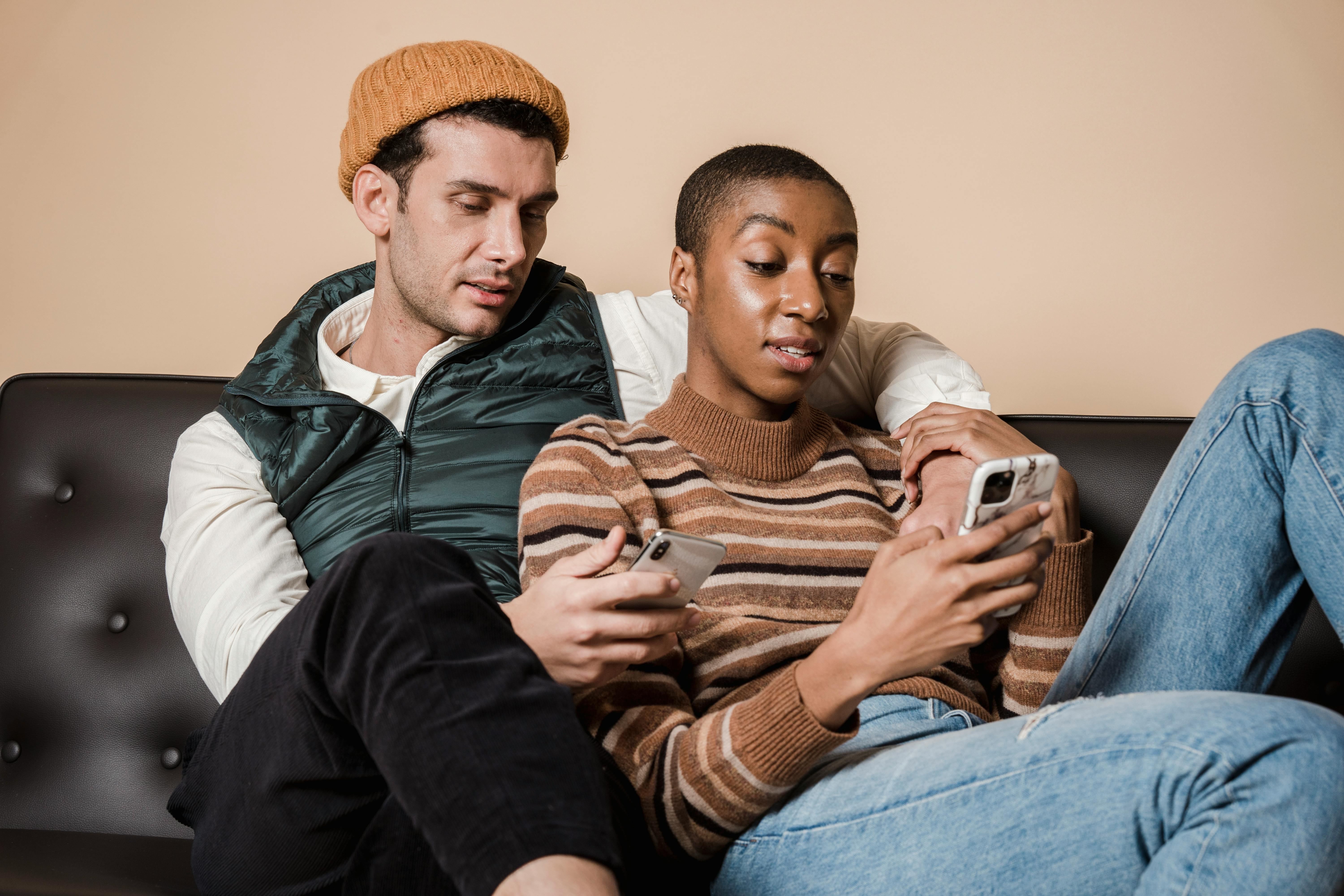 multiethnic couple browsing smartphones on couch