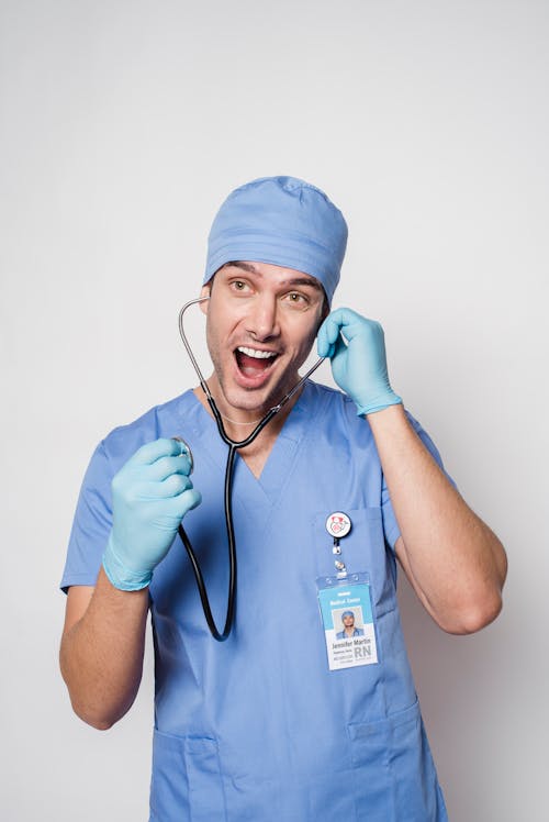 Free Amazed male medic in uniform and gloves with name tag putting stethoscope in ear and looking away with mouth opened Stock Photo