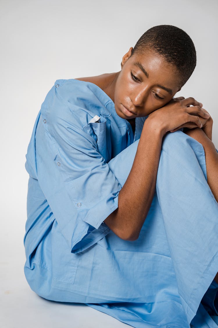 Upset Black Female Patient In Medical Robe Sitting On Floor