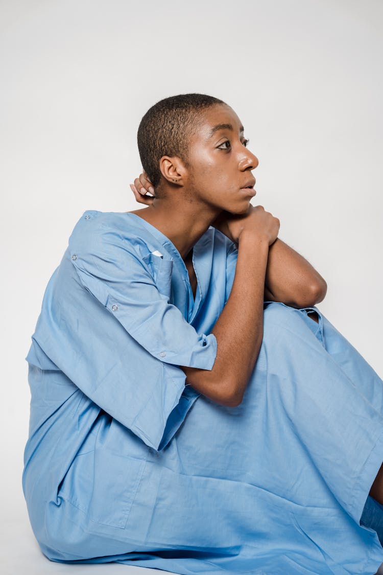 Thoughtful Black Woman In Medical Robe Sitting On Floor And Looking Away