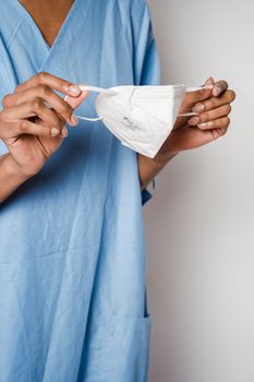 Crop faceless woman in blue medical uniform opening and wearing sterile respirator at hospital